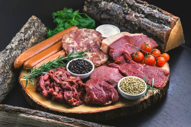 Przekrój mięs i kiełbas na desce z drewnianego pnia, zdrowa dieta, mięso i warzywa.